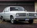 En vit, klassisk Plymouth Valiant står parkerad framför ett garage.