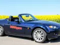 Blå Mazda MX-5 cabriolet parkerad vid en gul rapsåker. Ett potentiellt Mazda MX-5 problem kan vara att den drar till sig uppmärksamhet.