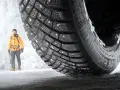 En man i gul jacka står framför en isvägg. Ett Continental IceContact 3-däck med dubb är i förgrunden, redo för test.