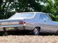 En grå Opel Diplomat coupé står parkerad utomhus.