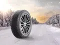 Michelin X-Ice Snow-däck på en snötäckt väg i en vinterskog. Solen bryter igenom molnen.