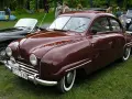 En vinröd Saab 92 står på gräs, med en svart cabriolet bredvid. Bilen har en klassisk design och en svensk registreringsskylt.