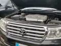 Motorhuven på en svart p0420 Toyota Land Cruiser är öppen, vilket visar V8-motorn. En annan likadan bil står bredvid.