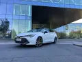 Vit Toyota Corolla Touring Sports framför en modern glasbyggnad. Inga problem med denna bil, bara ren stil.
