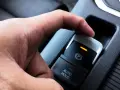 En hand trycker på knappen för elektronisk handbroms som låst sig. En orange lampa lyser.