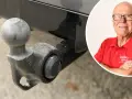 En man i röd tröja med texten "Tekniker Värld" ler, bredvid en bil med dragkrok. Dags att ta bort dragkrok?