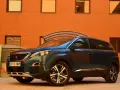 Mörkblå Peugeot 5008 SUV parkerad framför en orange tegelbyggnad. En perfekt bil för en familjeresa, en riktig peugeot 5008 test.