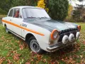Ford Taunus 12M i rallystuk, med orange detaljer och Castrol-logga, står på en gräsmatta täckt av höstlöv.