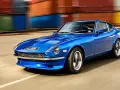 Blå Nissan Datsun 240Z kör förbi färgglada fraktcontainrar.