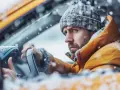 Man i gul jacka och mössa sitter i bil i snöstorm. Bilen startar inte, startmotorn går runt.