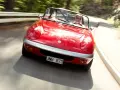 Röd Lotus Elan M100 körs på en kurvig väg genom en skog. Föraren bär solglasögon.