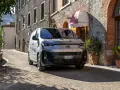 En grå Fiat Doblo står parkerad på en smal gata i Italien. En vacker byggnad med tegel och sten syns i bakgrunden.