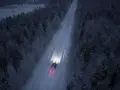 Bil kör på snöig skogsväg i mörker, halvljus symbolen lyser upp vägen.