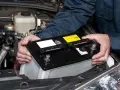 Mekaniker byter ett urladdat bilbatteri i motorutrymmet.