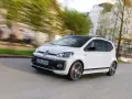 Vit VW Up GTI med svarta detaljer kör genom en stad.