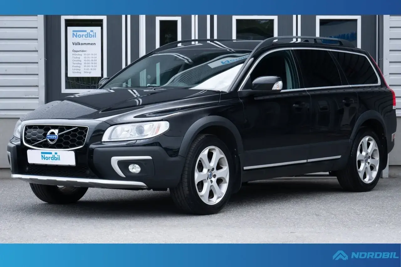 Svart Volvo XC70 parkerad framför en byggnad med skylten "Nordbil Välkommen". Bilen har takräcken och en robust design.