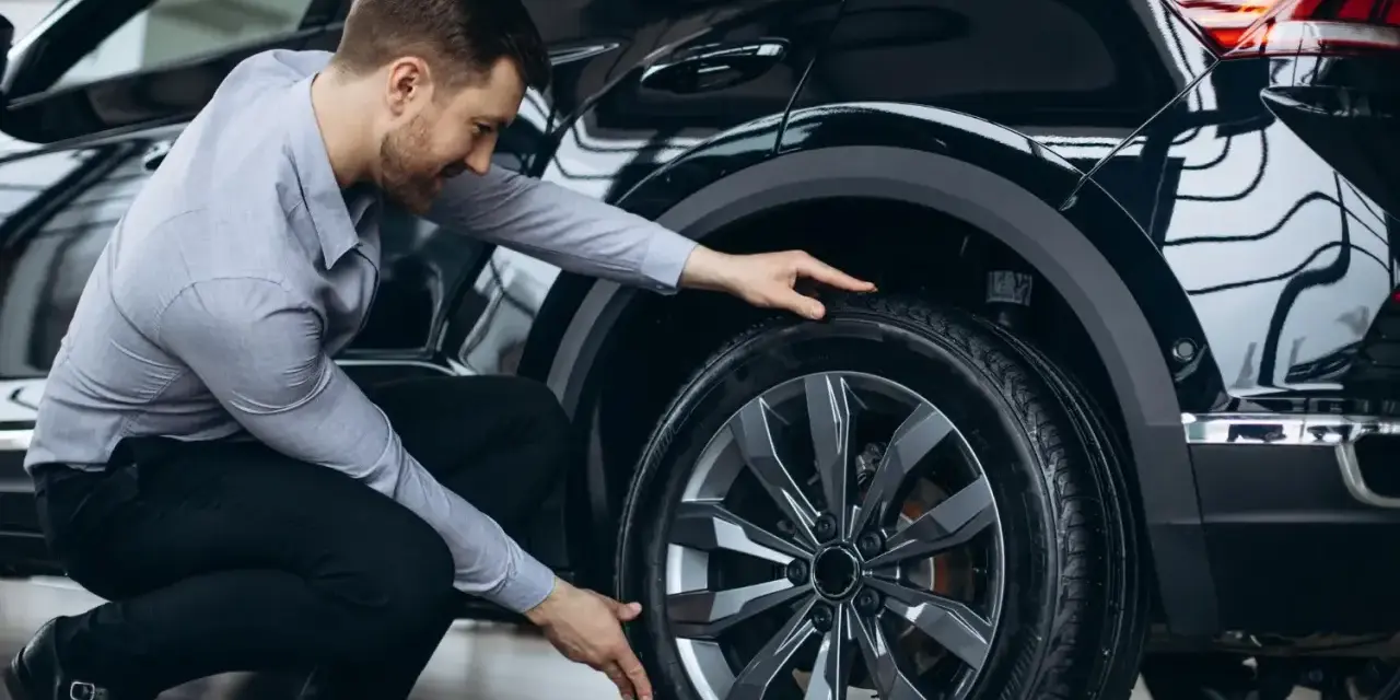 Man inspekterar däcket på en svart bil, redo för ett kumho ecsta ps71 test.