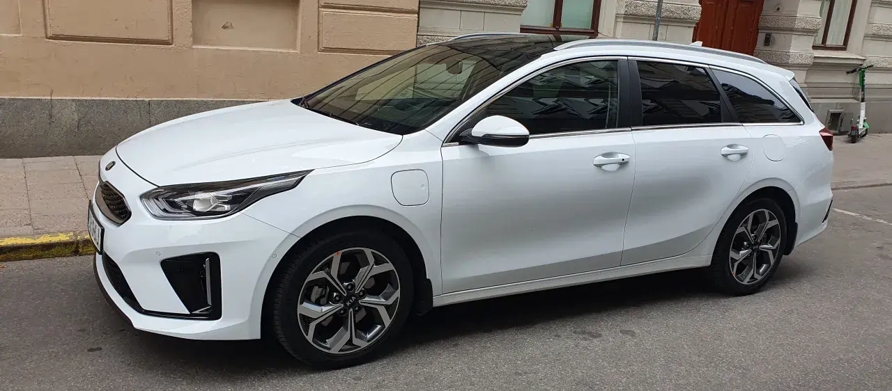 Vit Kia Ceed SW Plug-in Hybrid parkerad på gata. En elsparkcykel syns i bakgrunden.