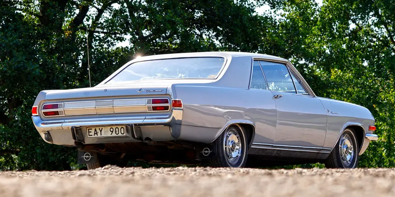 En grå Opel Diplomat coupé står parkerad utomhus.