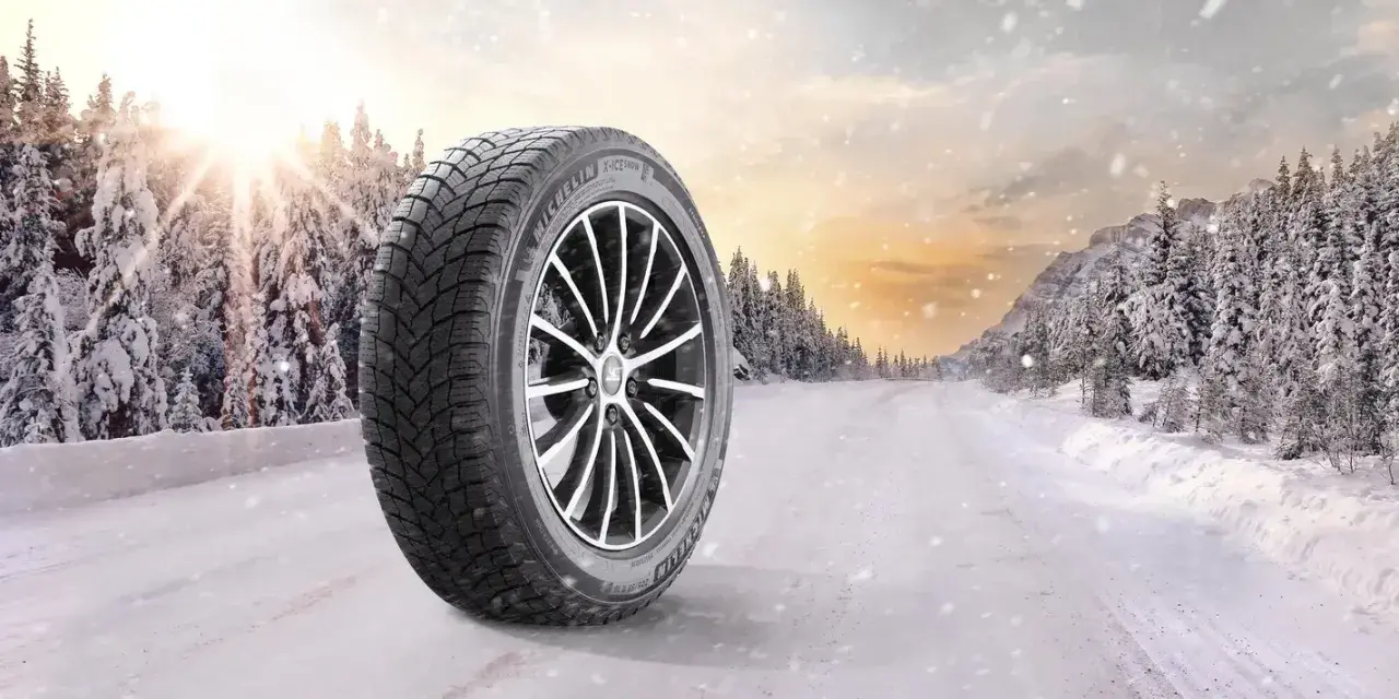 Michelin X-Ice Snow-däck på en snötäckt väg i en vinterskog. Solen bryter igenom molnen.