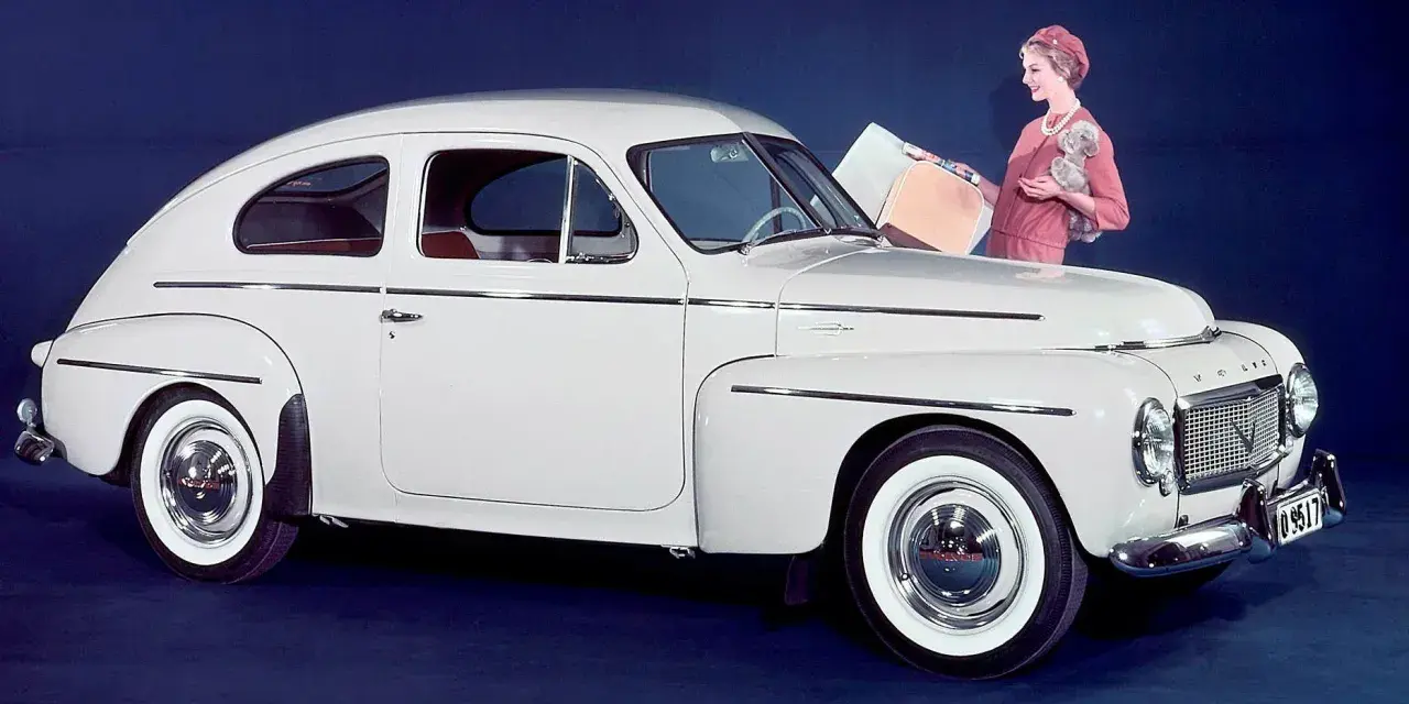 En elegant vit Volvo PV 444 med en kvinna och en hund bredvid.