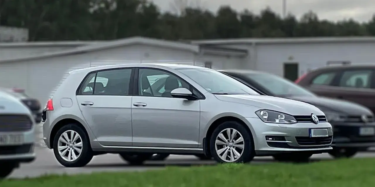 Silver Golf sportsvan parkerad på gräs. En mörkare bil syns bakom.