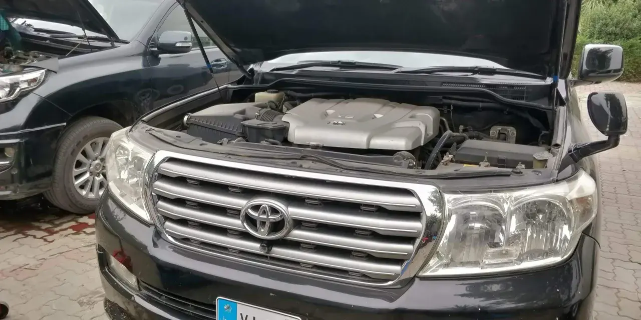 Motorhuven på en svart p0420 Toyota Land Cruiser är öppen, vilket visar V8-motorn. En annan likadan bil står bredvid.