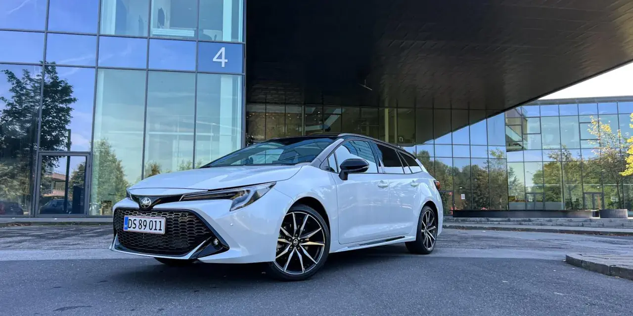 Vit Toyota Corolla Touring Sports framför en modern glasbyggnad. Inga problem med denna bil, bara ren stil.
