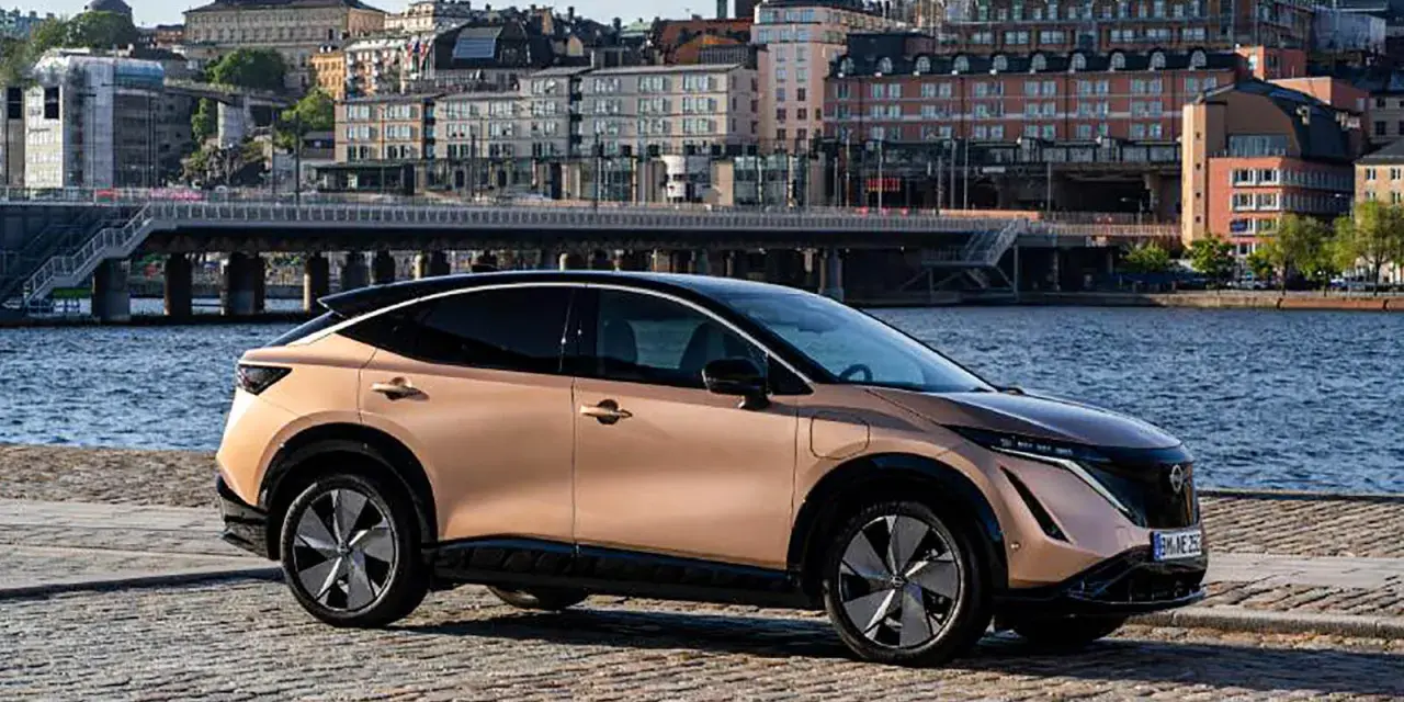 Nissan Ariya testkörning i Stockholm. En elegant elbil parkerad vid vattnet med stadens silhuett i bakgrunden.
