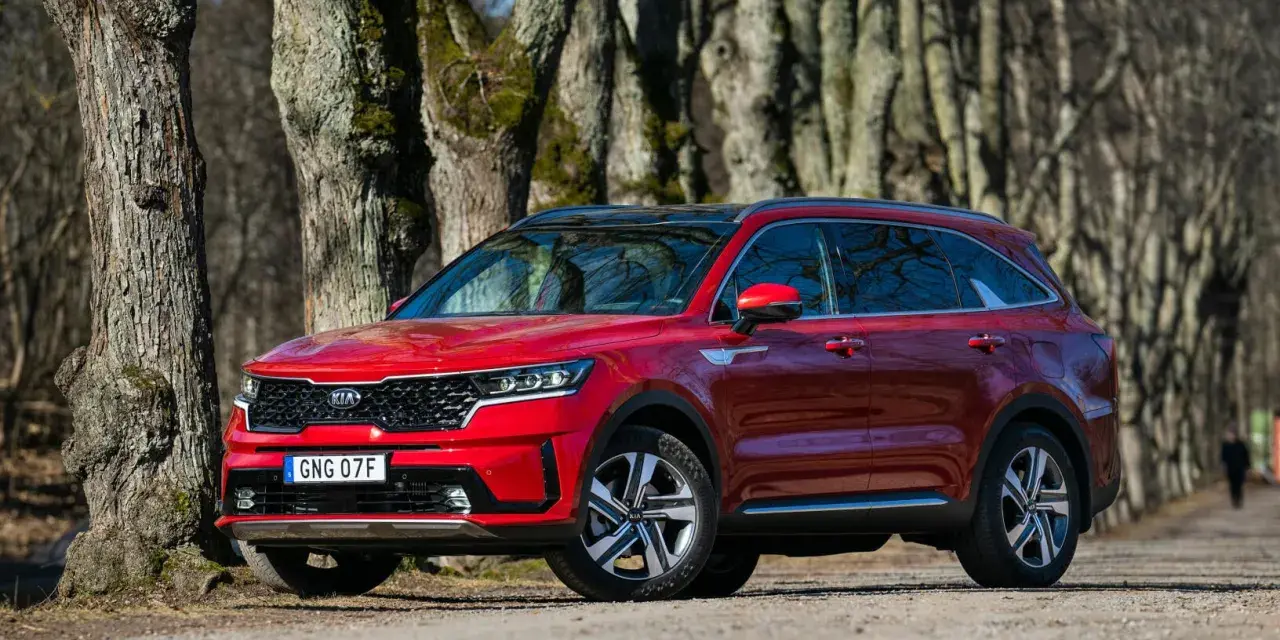 Röd Kia Sorento parkerad längs en trädkantad grusväg. En person syns i bakgrunden, kanske på väg att undersöka ett eventuellt kia sorento problem.