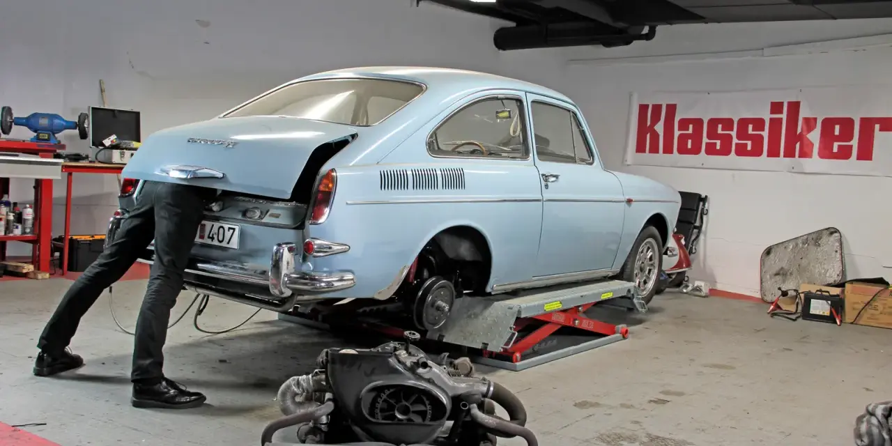 Mekaniker arbetar med en ljusblå vw typ 3 i verkstad. Motorn ligger framför bilen.