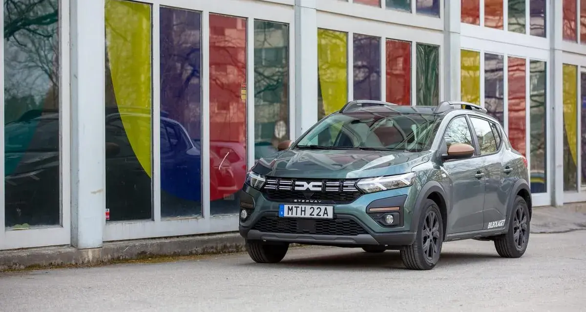 Grön Dacia Sandero Stepway, redo för ett däcktest. Bilen står parkerad framför en byggnad med färgglada fönster.