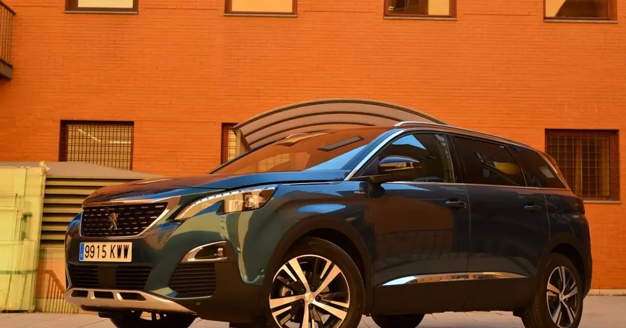 Mörkblå Peugeot 5008 SUV parkerad framför en orange tegelbyggnad. En perfekt bil för en familjeresa, en riktig peugeot 5008 test.