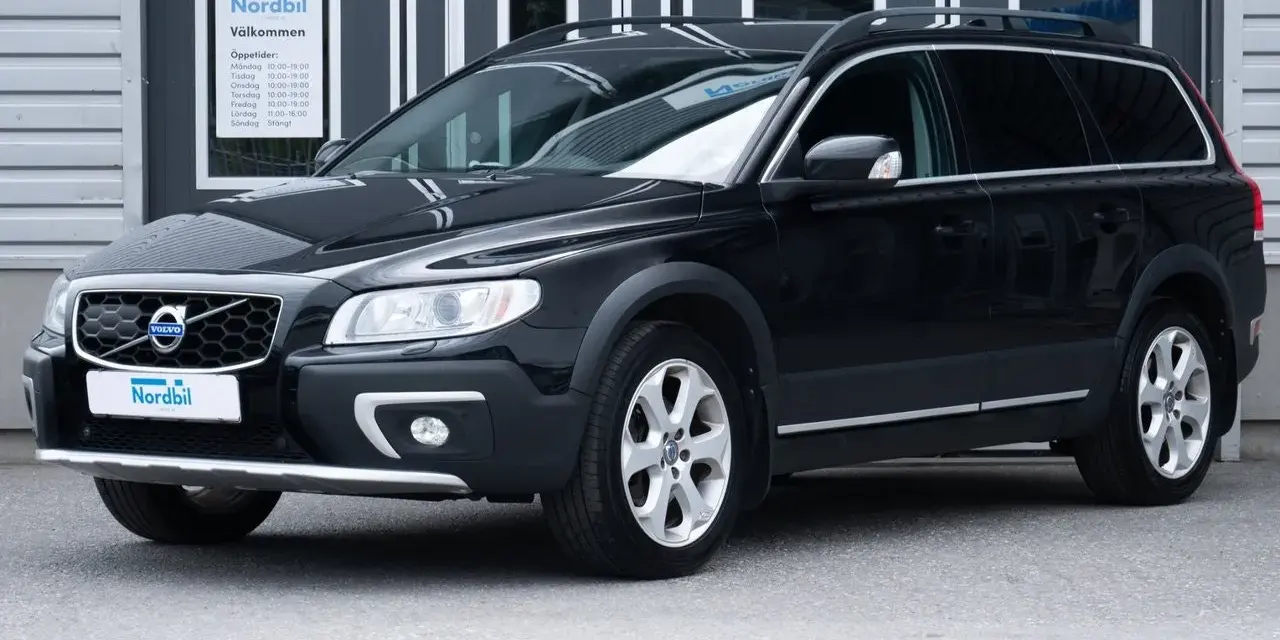 Svart Volvo XC70 parkerad framför en byggnad med skylten "Nordbil Välkommen". Bilen har takräcken och en robust design.