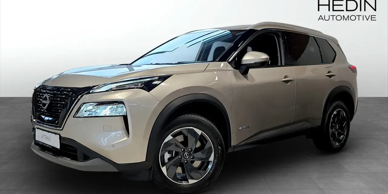 A tan Nissan X-Trail e-POWER SUV is shown from the front three-quarter view in a showroom.