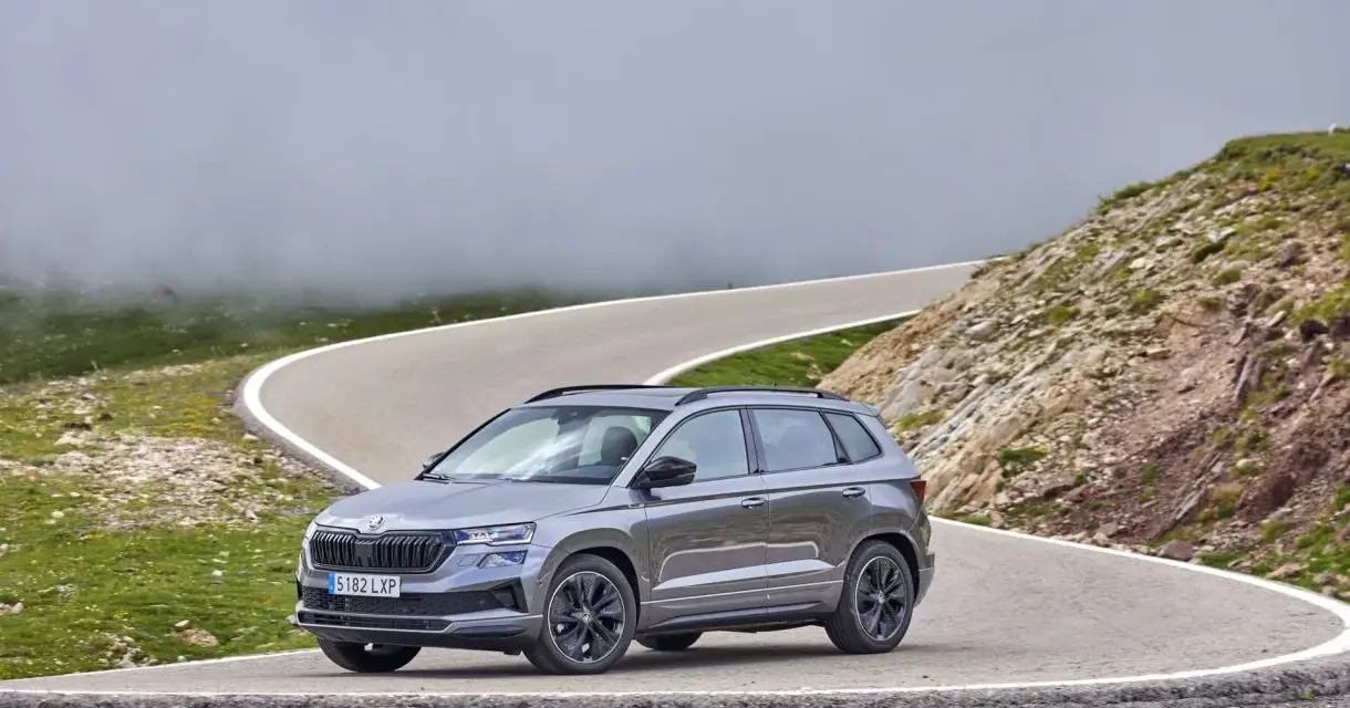 Grå Skoda Karoq på en slingrig bergsväg, omgiven av dimma och grönska. Inga problem här, bara en vacker utsikt.