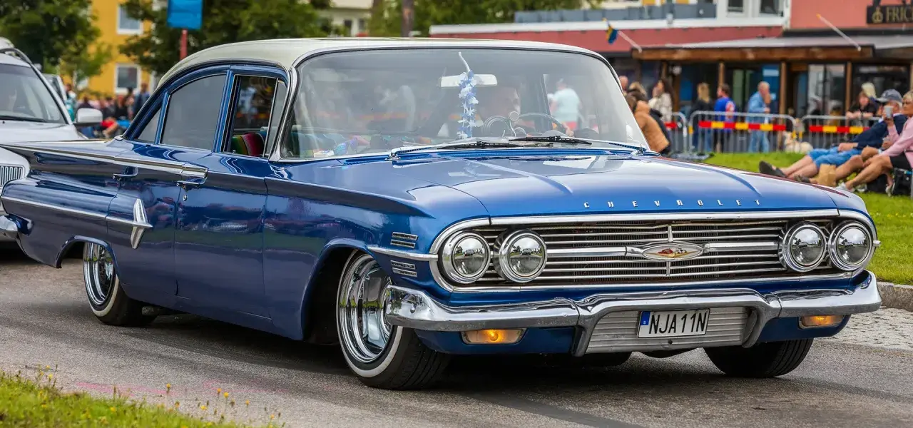 En blå klassisk bil, en Chevrolet, rullar fram på en gata.