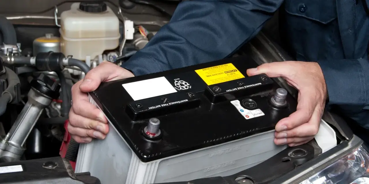 Mekaniker byter ett urladdat bilbatteri i motorutrymmet.