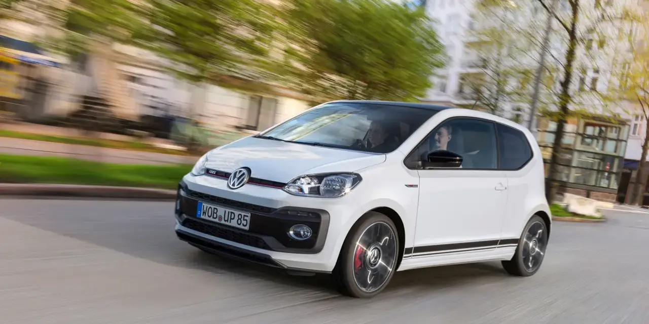 Vit VW Up GTI med svarta detaljer kör genom en stad.