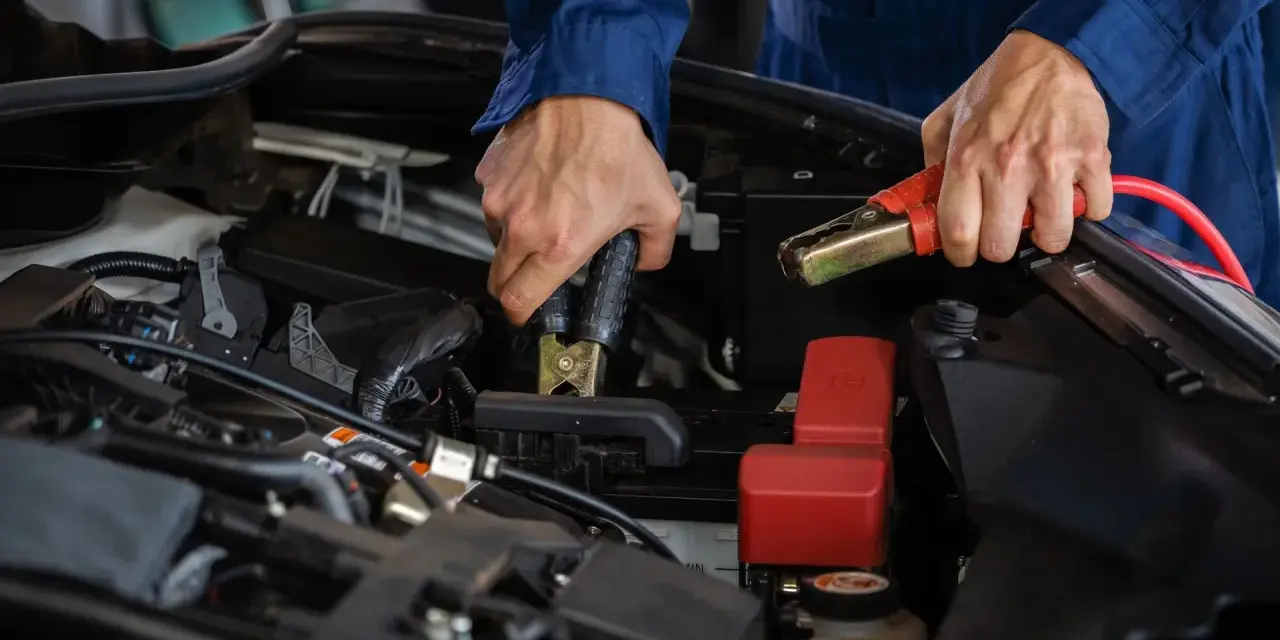 Mekaniker kopplar startkablar till bilbatteriet. Frågan "hur lång tid tar det att ladda ett bilbatteri" är relevant här.