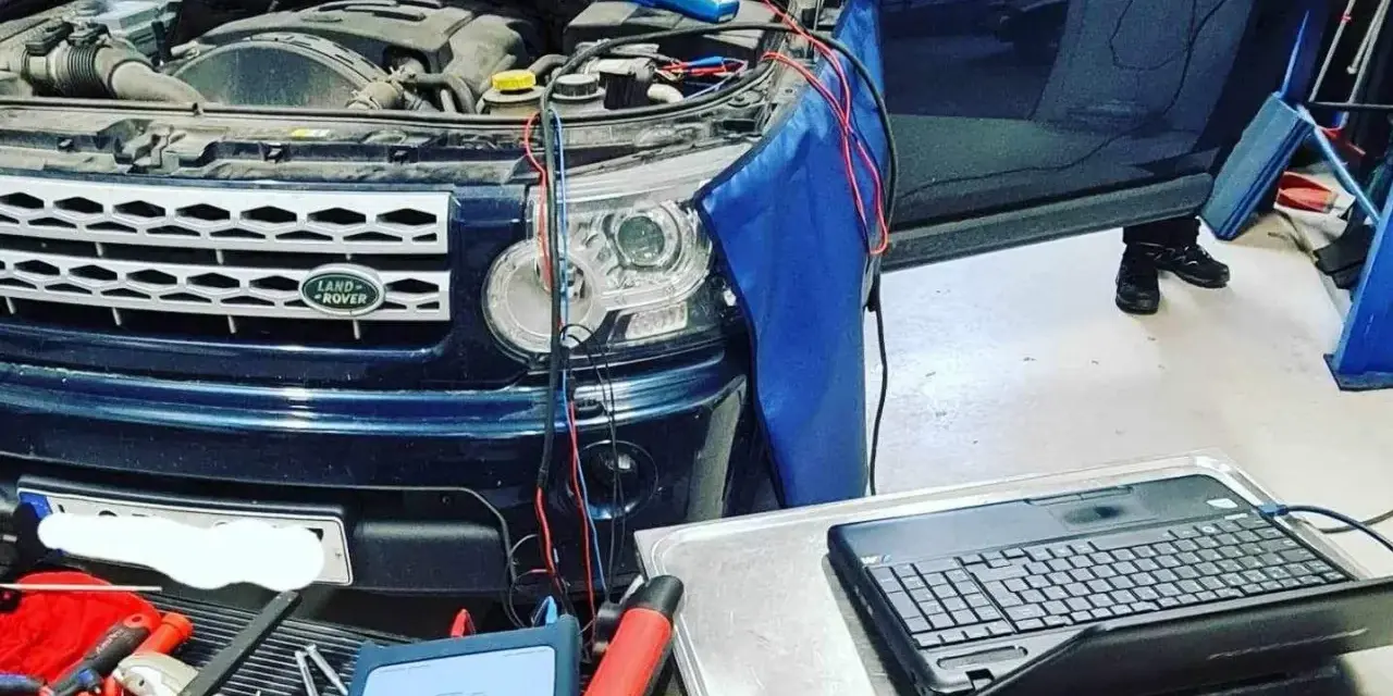 Diagnostik av Land Rover med öppen motorhuv. Kablar kopplade till motor och en dator för felsökning av jordfel bil symtom.