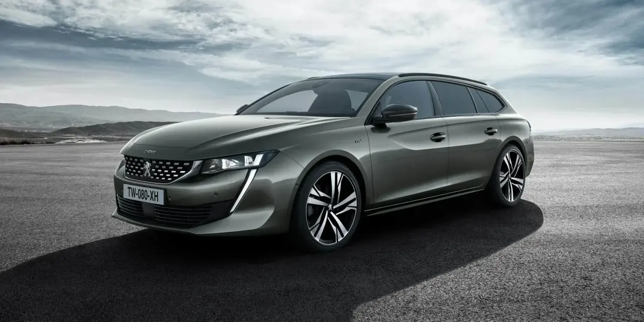 Grå Peugeot 508 SW står parkerad på en asfalterad yta med berg i bakgrunden. En perfekt bil för ett peugeot 508 test.
