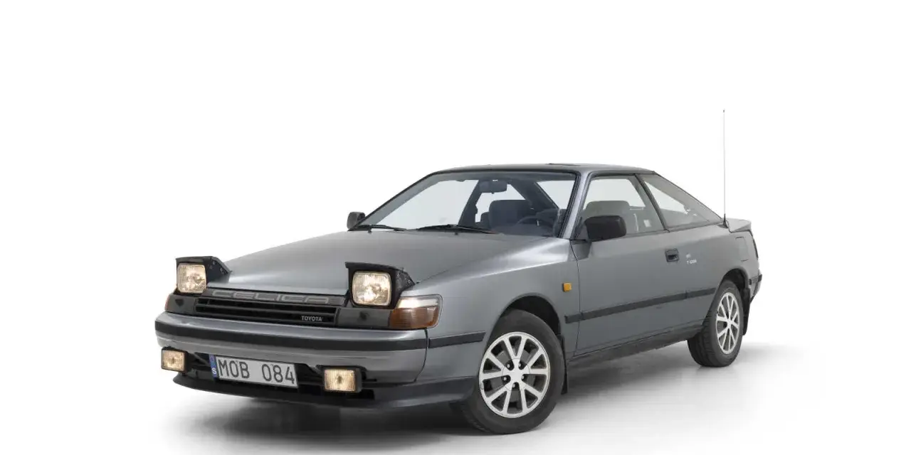 Grå Toyota Celica 1986 med pop-up-strålkastare, redo för en nostalgisk resa.