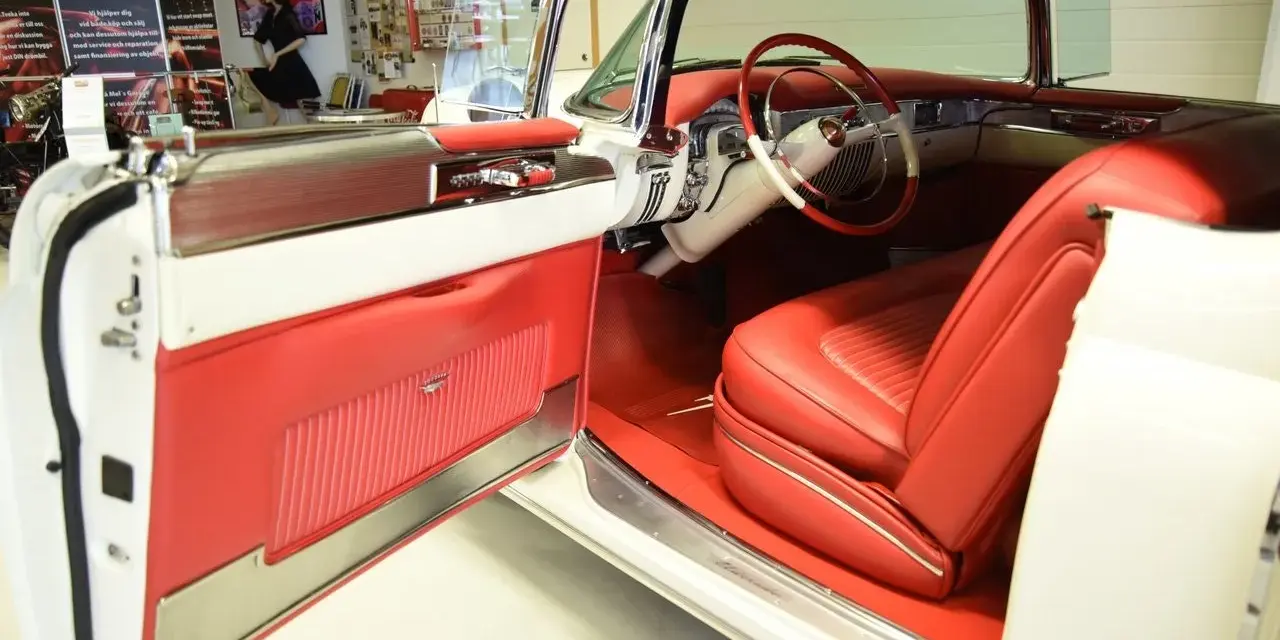 En vit cabriolet Cadillac från 50-talet med lyxig röd interiör. Dörren är öppen och visar upp säten och instrumentbräda.