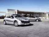 Två silverfärgade Peugeot 207 CC cabriolet står parkerade på en stenlagd uteplats framför en modern byggnad.