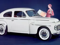 En elegant vit Volvo PV 444 med en kvinna och en hund bredvid.
