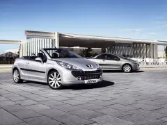 Två silverfärgade Peugeot 207 CC cabriolet står parkerade på en stenlagd uteplats framför en modern byggnad.