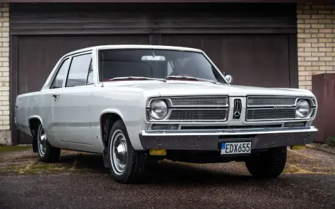 En vit, klassisk Plymouth Valiant står parkerad framför ett garage.