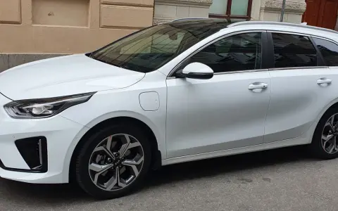 Vit Kia Ceed SW Plug-in Hybrid parkerad på gata. En elsparkcykel syns i bakgrunden.