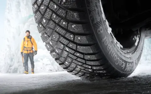 En man i gul jacka står framför en isvägg. Ett Continental IceContact 3-däck med dubb är i förgrunden, redo för test.